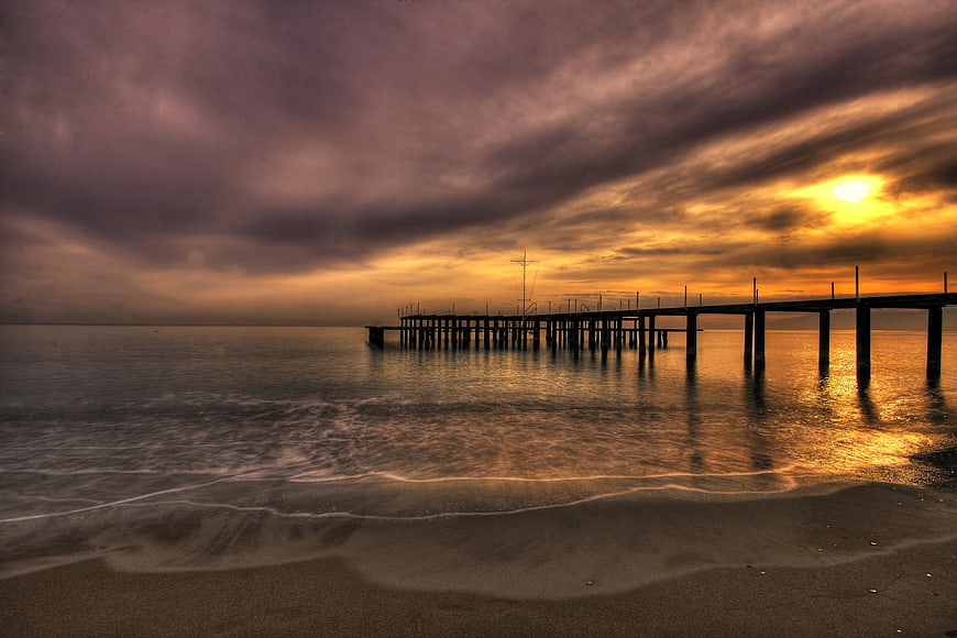 Dramatic Sunset Over Ocean Pier With Moody Clouds