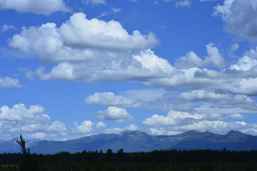 Blue sky with white clouds over mountain range and forest