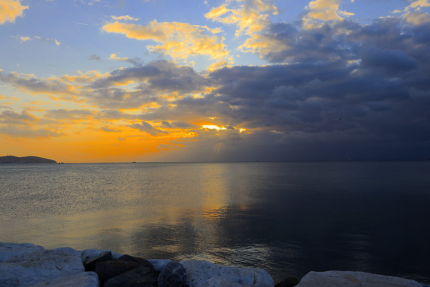 Dramatic Sunset Over Calm Sea with Golden Clouds and Rocky Foreground