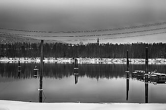 Serene black and white winter lake with dock posts and reflection