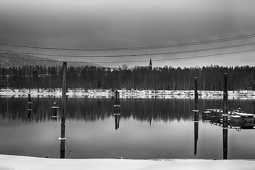 Serene black and white winter lake with dock posts and reflection