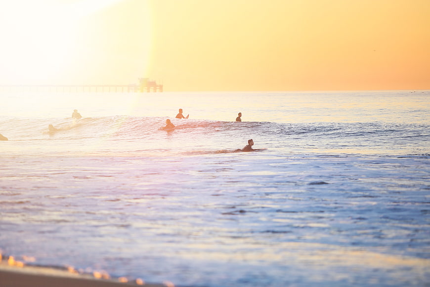 Surfers paddling in ocean waves during golden sunset