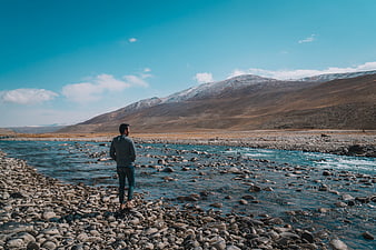 Man Standing by River in Mountain Landscape