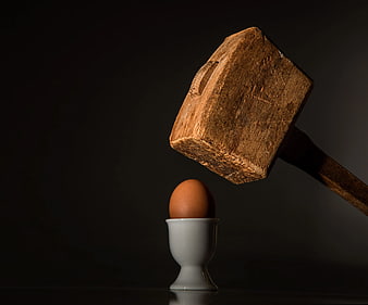 Wooden Mallet Hovering Over Brown Egg in Cup