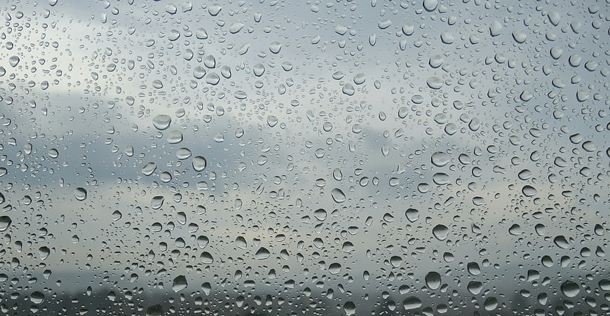 Raindrops on Glass Window with Blurred Gray Sky Background