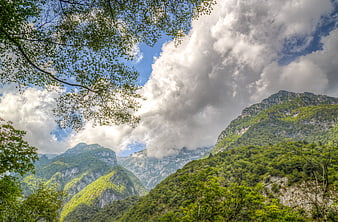 Lush green mountain valley with dramatic clouds and blue sky