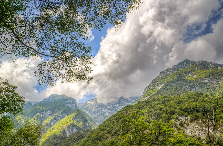 Lush green mountain valley with dramatic clouds and blue sky
