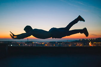 Silhouette of man jumping on rooftop at sunset