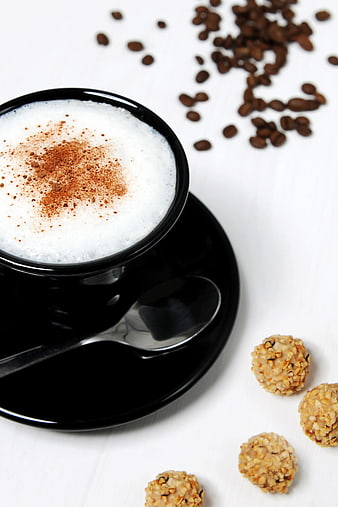 Black cup of frothy cappuccino with oat balls and coffee beans