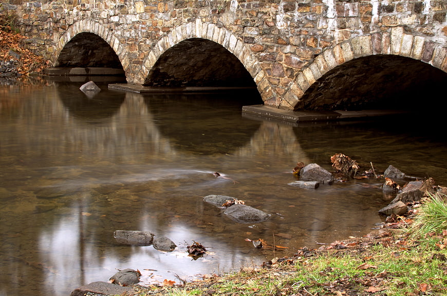 Old stone bridge over calm river in autumn
