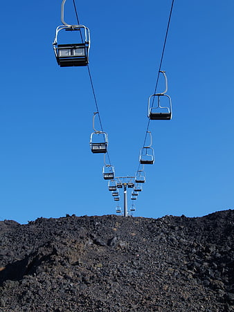 Empty ski lift chairs against blue sky over volcanic rock