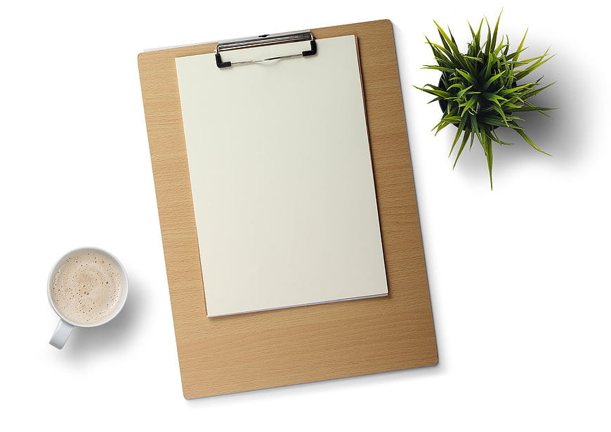 Top view of clipboard with blank paper, coffee, and plant on white background