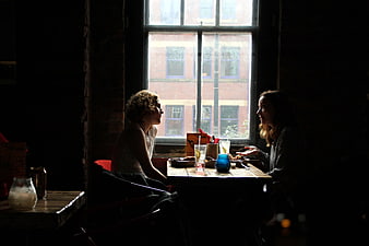 Two Women Having Lunch Conversation In Dark Cafe By Window