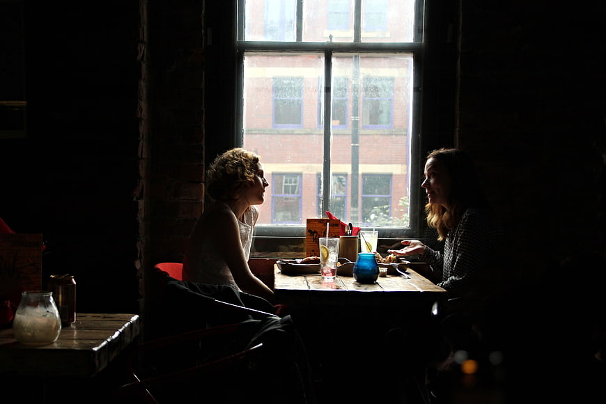Two Women Having Lunch Conversation In Dark Cafe By Window