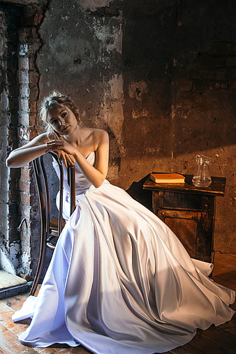 Young woman in white wedding dress sitting in rustic room