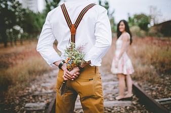 Man Holding Bouquet Behind Back on Railroad Tracks