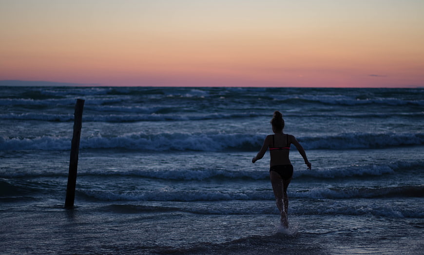 Woman Running into Ocean Waves at Sunset