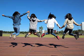 Four girls jumping in a park holding hands