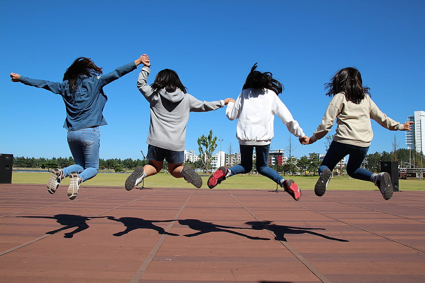 Four girls jumping in a park holding hands