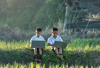 Two young boys using laptops in a rural field