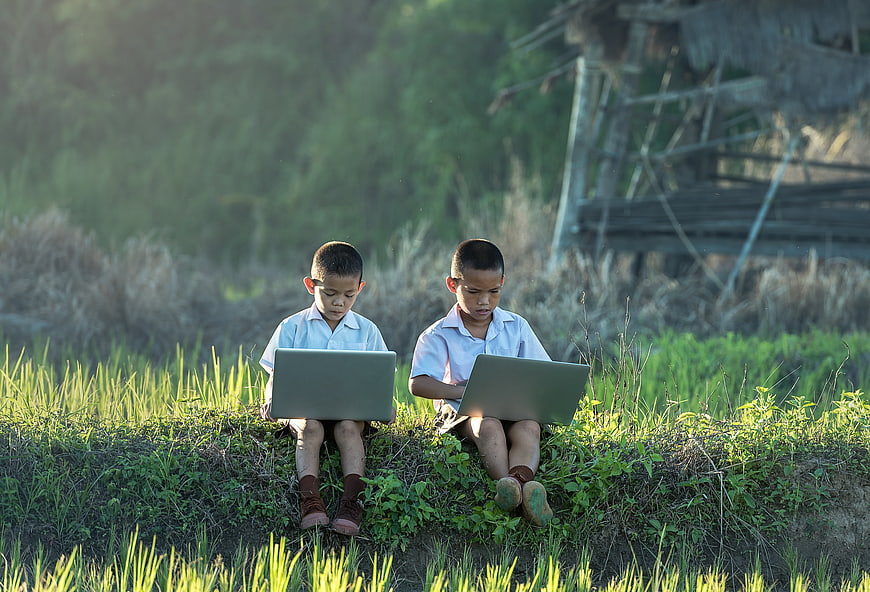 Two young boys using laptops in a rural field