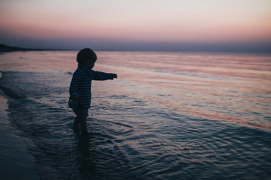 Toddler Boy Playing in Ocean Waves at Sunset