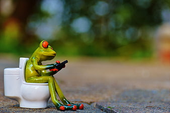 Cute Green Frog Figurine Sitting on Miniature Toilet Holding Smartphone
