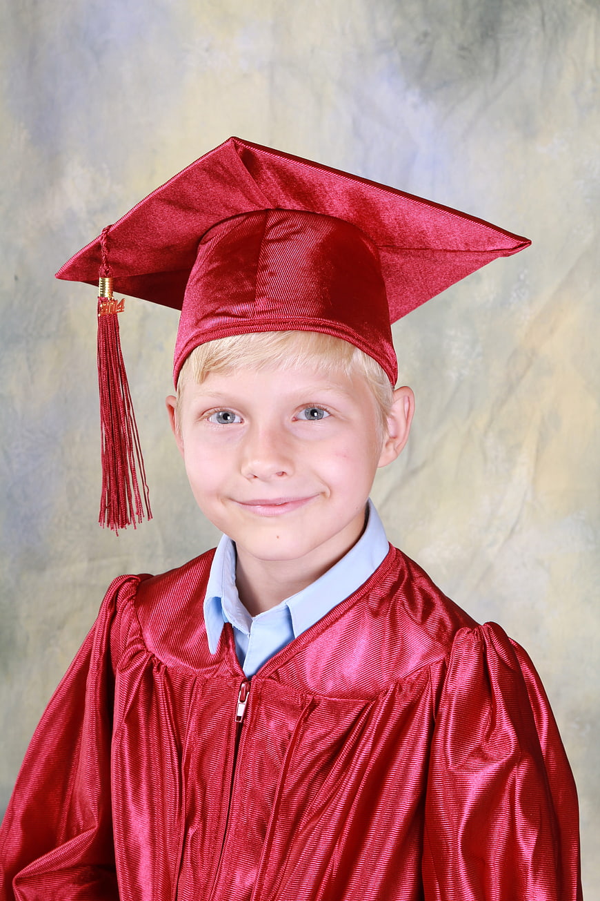 Happy young boy in red graduation cap and gown