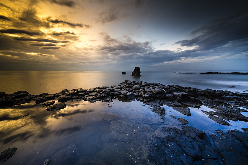 Dramatic Sunset Over Rocky Coastline with Tide Pool Reflection