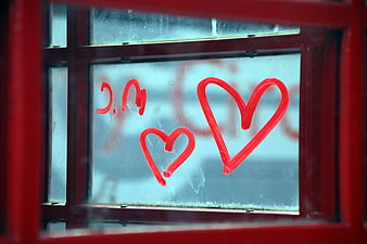 Red hearts drawn on foggy window glass