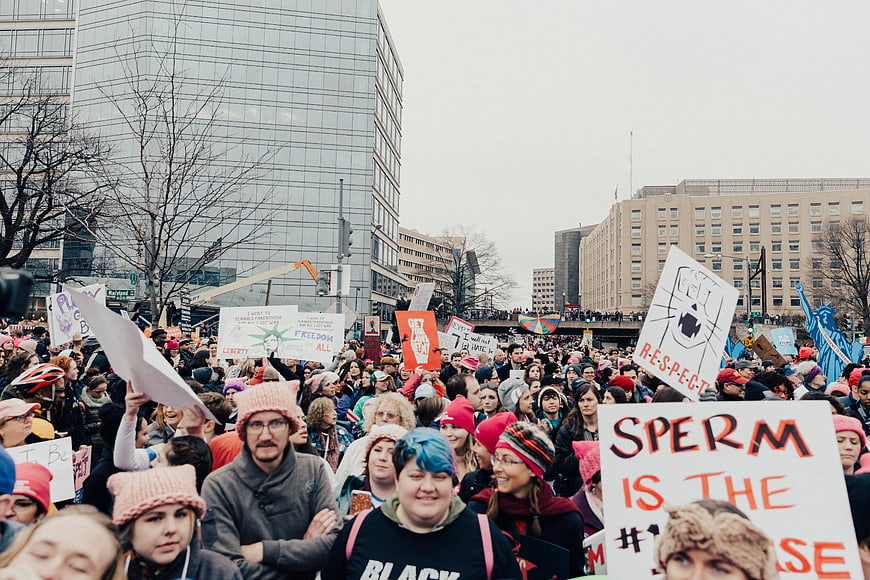 Crowd at urban protest rally holding signs and wearing pink hats