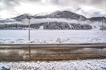 Wet road with snowy mountains and misty forest background
