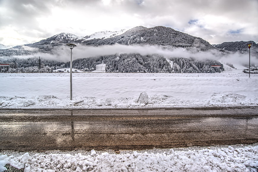 Wet road with snowy mountains and misty forest background
