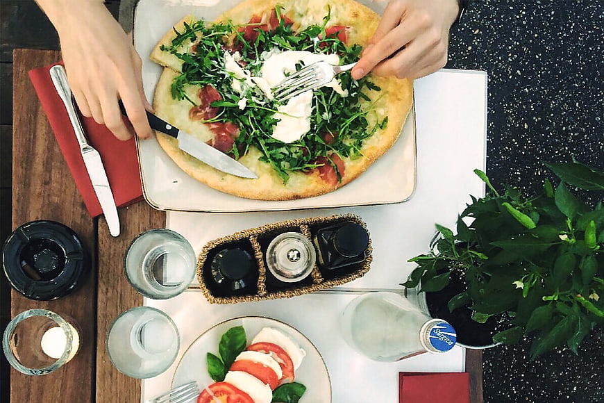 Overhead view of fresh pizza with arugula and burrata being cut