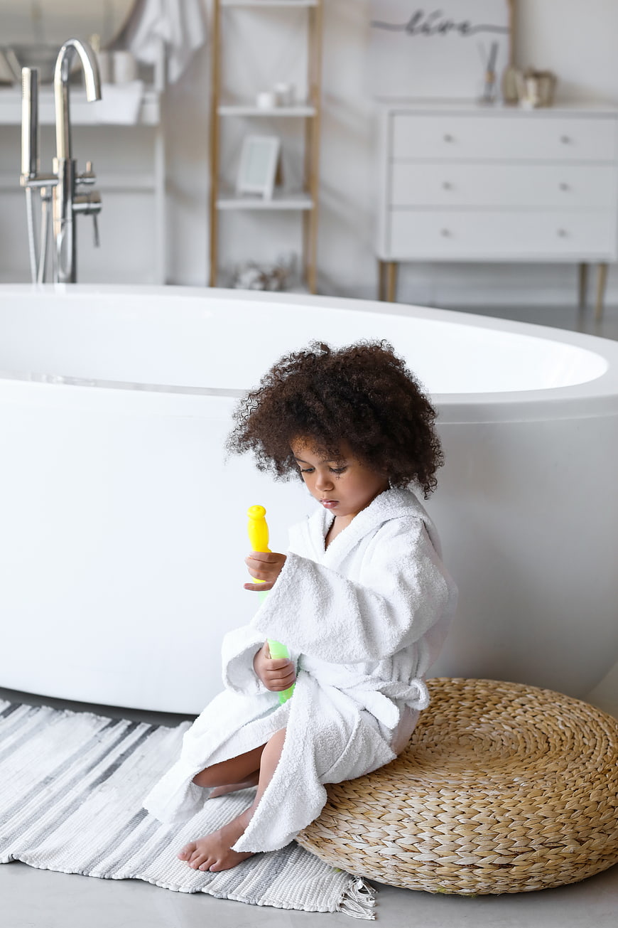 Cute Child in White Robe Playing with Toys in Bathroom