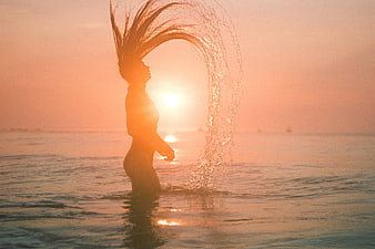 Woman whipping wet hair in ocean at sunset