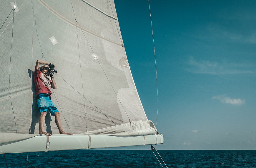 Man taking photo on sailboat deck against blue sky