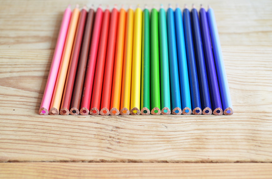 Rainbow colored pencils arranged on wooden background
