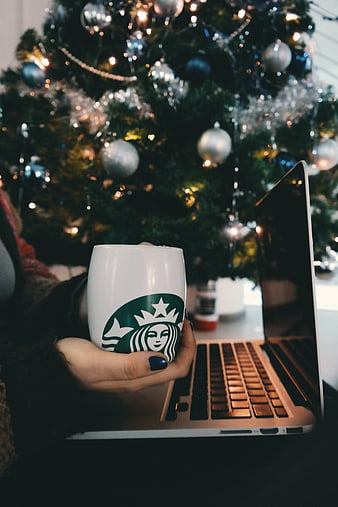 Woman holding Starbucks mug near laptop with Christmas tree background
