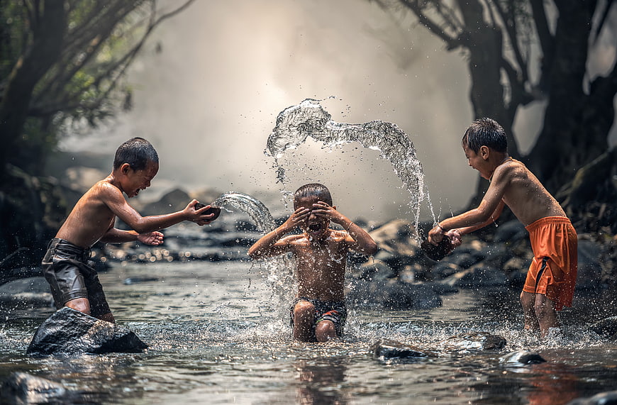 Three boys splashing water in a river