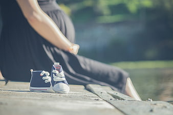 Pregnant woman sitting with baby shoes on wooden dock