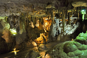 Illuminated limestone cave interior with stalactites and underground stream