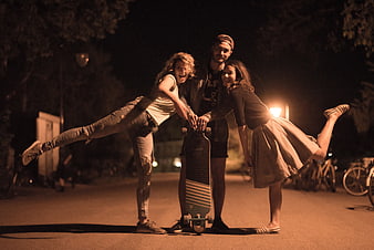 Three friends posing with longboard at night in urban park
