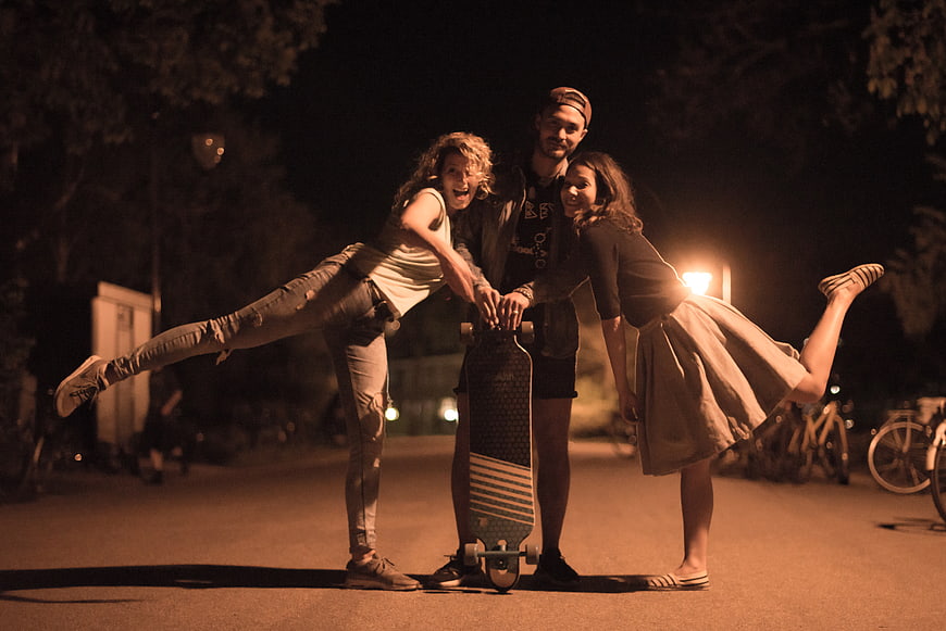 Three friends posing with longboard at night in urban park