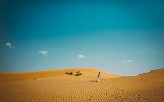 Lone Traveler Walking on Golden Sand Dunes Under Blue Sky