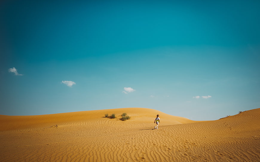 Lone Traveler Walking on Golden Sand Dunes Under Blue Sky
