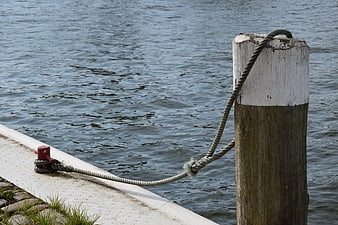Weathered Wooden Mooring Post With Rope On Waterfront