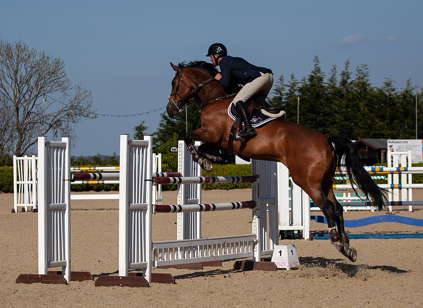 Equestrian rider jumping horse over obstacle in show jumping arena