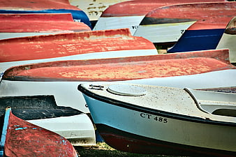 Weathered red and white boats stacked on grass