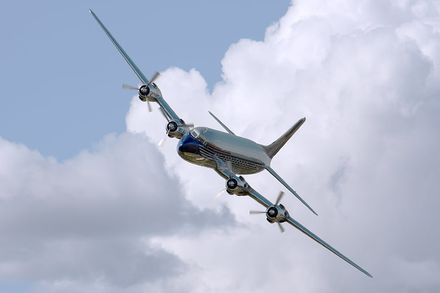 Vintage Silver Propeller Airplane Flying in Blue Sky